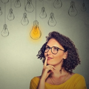 Thinking woman in glasses looking up with light idea bulb above head isolated on gray wall background-159976-edited.jpeg